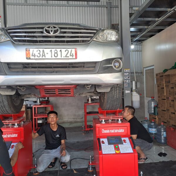 Hai kỹ thuật viên đưa cụm Chassis road simulator vào dưới gầm xe Toyota Fortuner đang nâng trên cầu